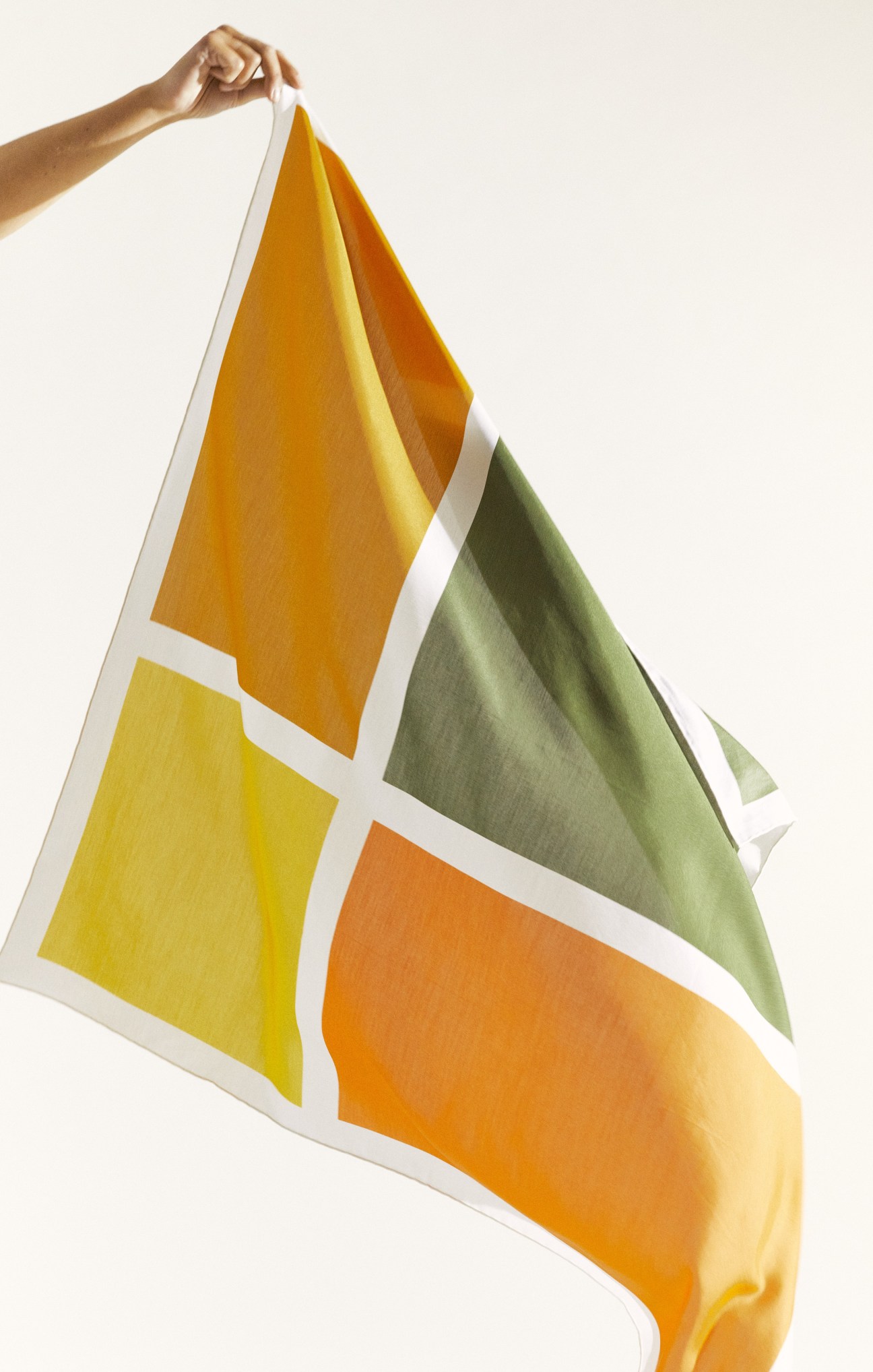 Hand holding Les Belles Heures × Konfekt silk scarf with geometric color-block pattern in yellow, orange and green