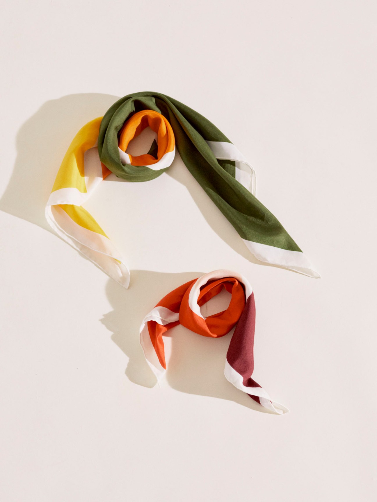 Two silk scarves with color-block patterns in yellow-green-orange and orange-burgundy combinations