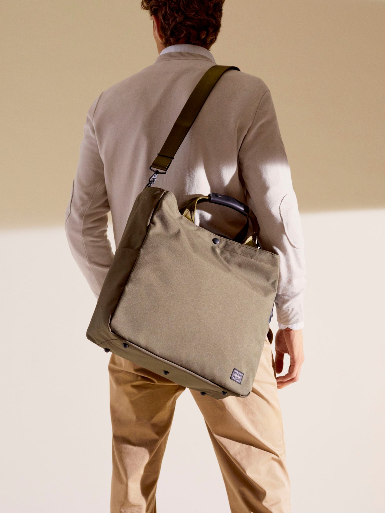 Person wearing olive Porter tote bag with zip closure and shoulder strap across body