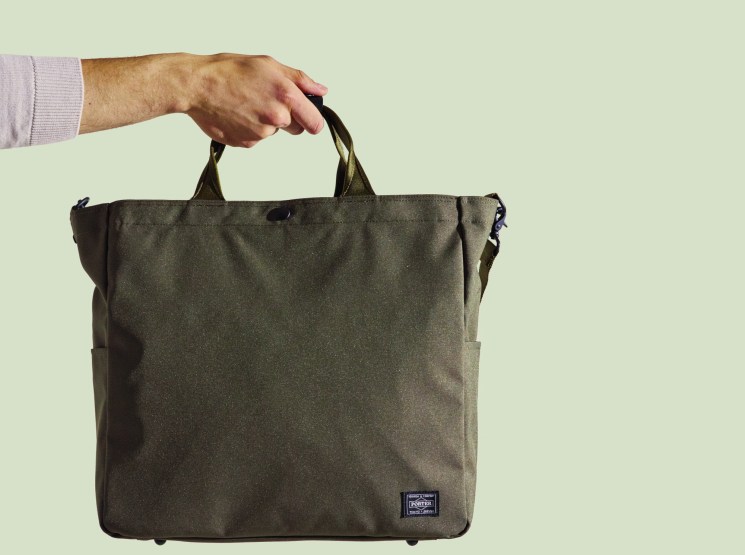 Porter × Monocle zip tote in olive being held by a hand against a pale green background.