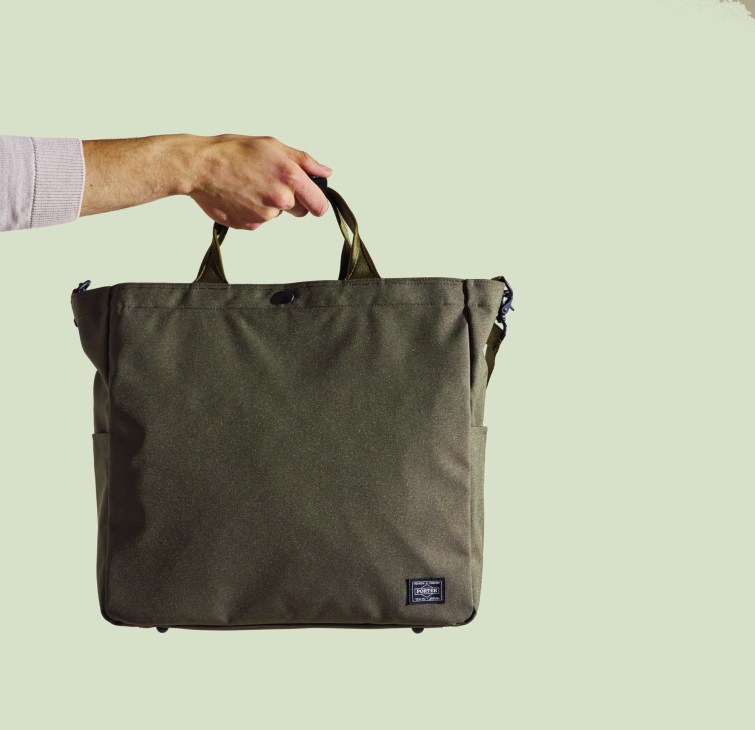 Porter × Monocle zip tote in olive being held by a hand against a pale green background.