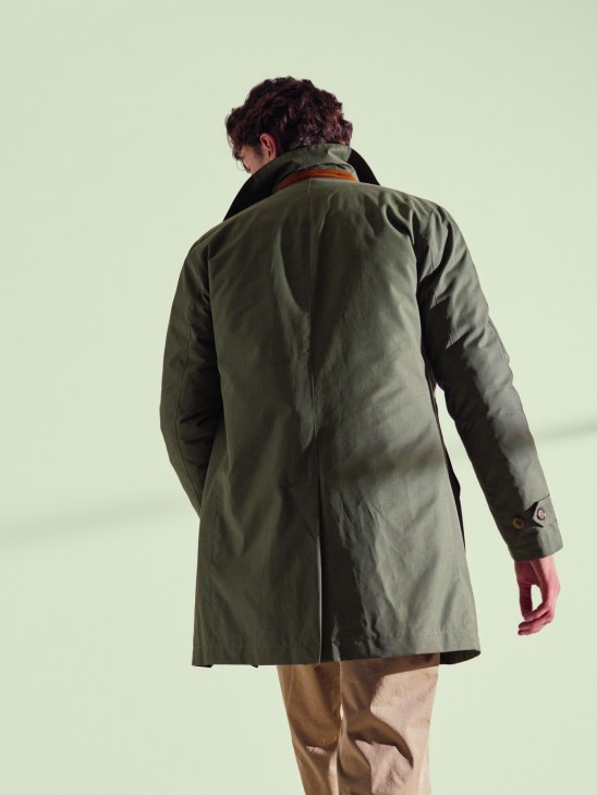 Model wearing Valstar × Monocle Milano raincoat in olive with detachable goose-down insert, shown from behind.