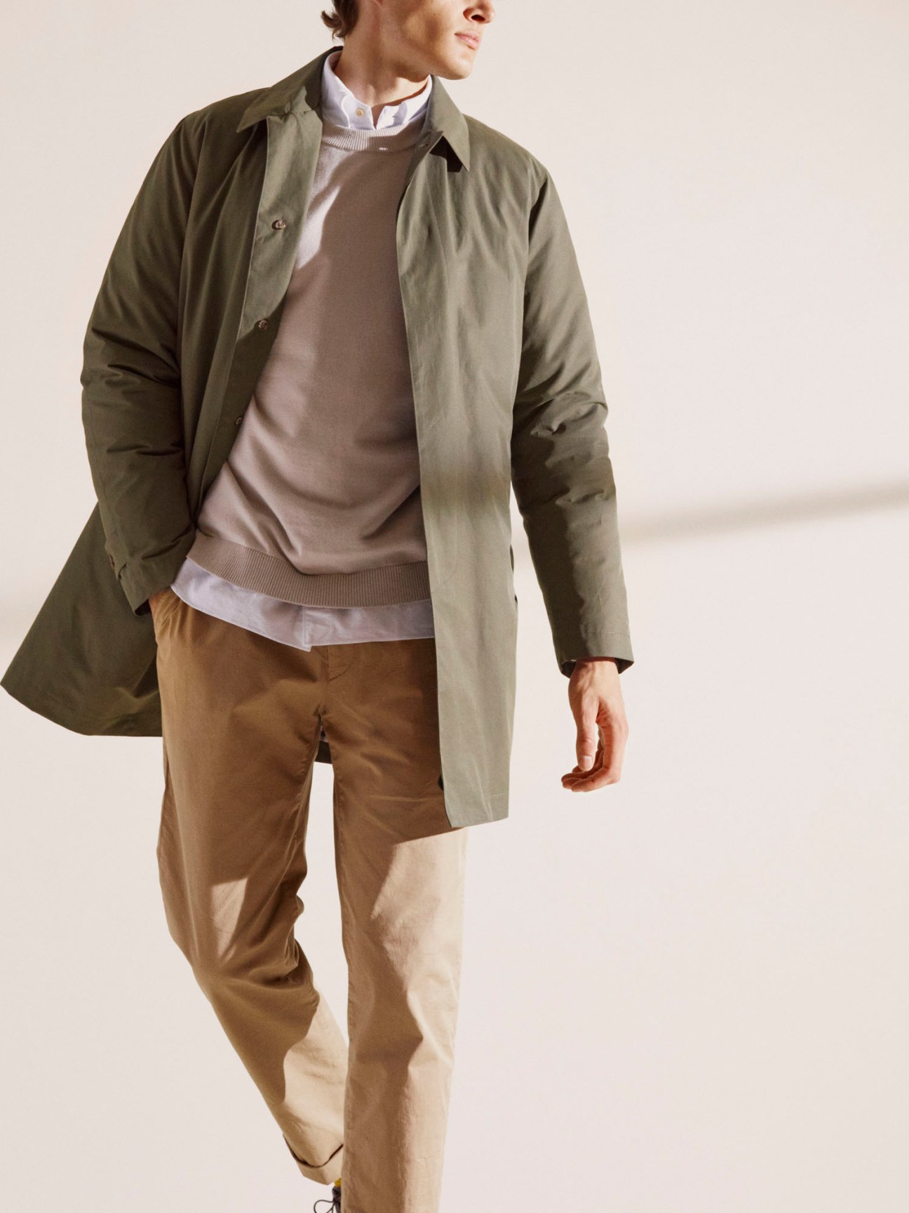 Man wearing olive green Valstar raincoat with layered sweater and chinos in neutral tones