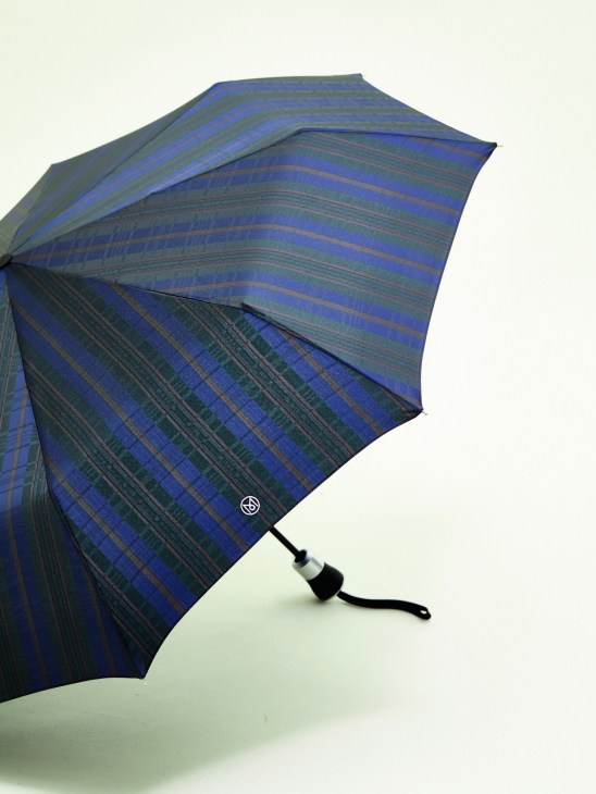 Doppler × Monocle carbon-steel umbrella with olive-and-blue check canopy, open against a pale background.