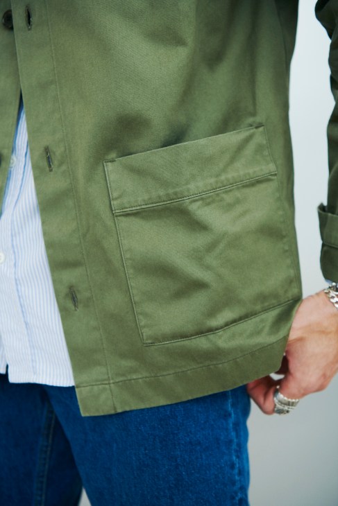 Close-up of Asket overshirt in sage green with visible cargo pocket and buttons.