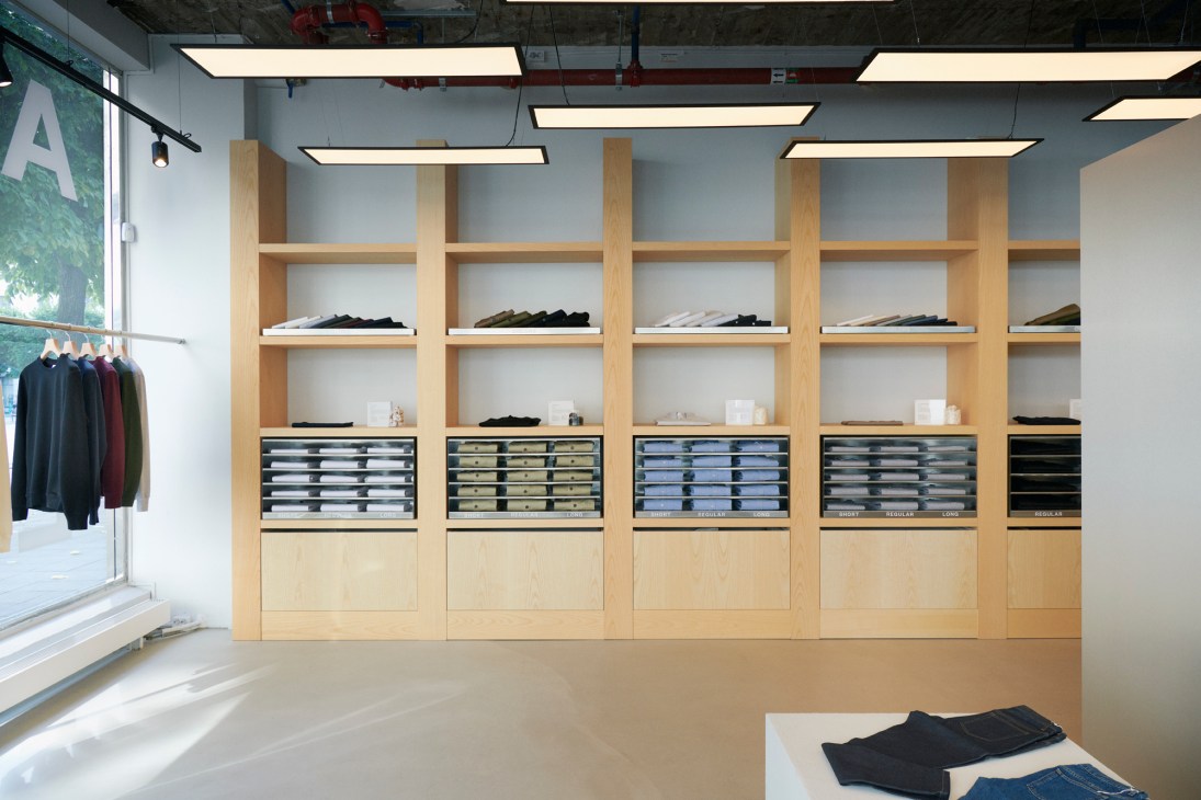 Interior of Asket's Stockholm shop with wooden shelving displaying folded basics and organized drawers.