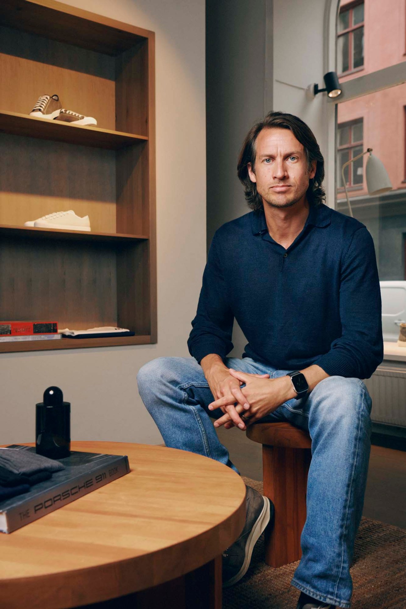 Adam Lewenhaupt, founder of CQP, sitting in a minimalist office with shelving displaying sneakers behind him.