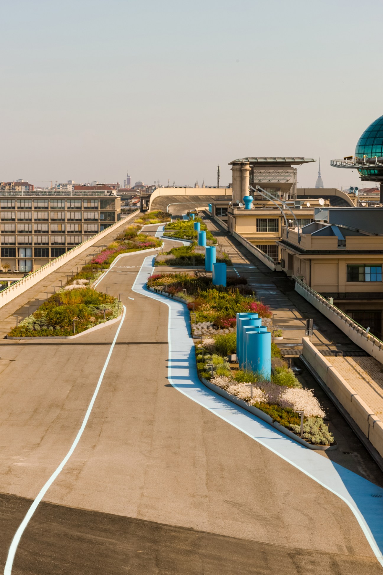 La Pista 500 rooftop garden with curved walking track, scattered planted islands and blue pillars on Turin's Lingotto building