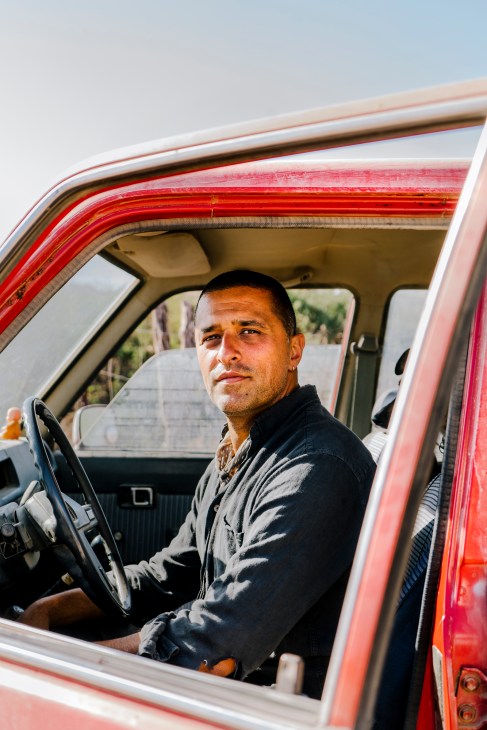Man sitting in driver's seat of red pickup truck looking toward camera