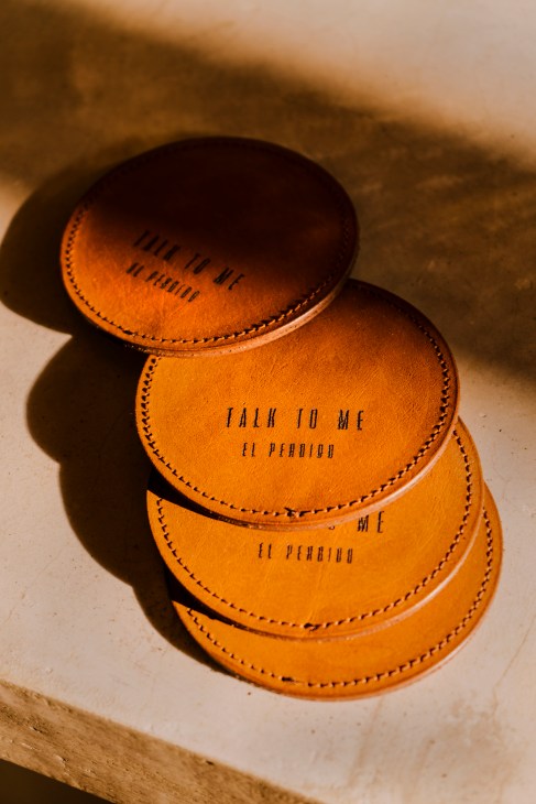 Stack of tan leather coasters with Spanish text and stitched edges at El Perdido hotel.