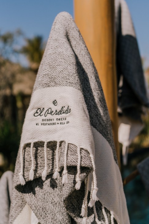 El Perdido hotel towel with desert dream branding draped over a yellow post by the pool