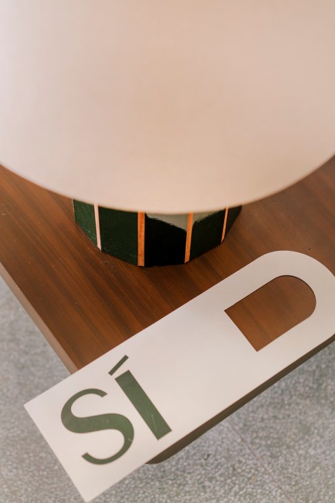 Detail shot of a wooden architectural element with inlaid green and orange stripes and a white card labeled 'si'.