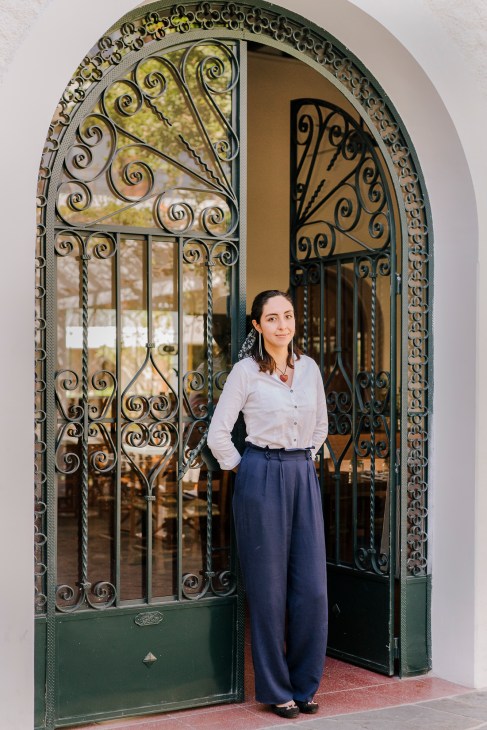 Fernanda, a hostess at Baja Club hotel in La Paz, stands in a decorative arched doorway with ornate wrought iron detailing.