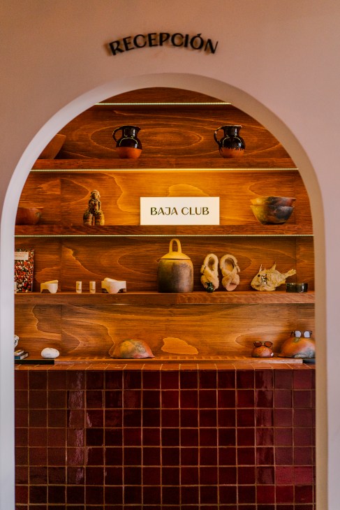 Baja Club hotel reception desk with wooden shelving displaying artisanal crafts and accessories.
