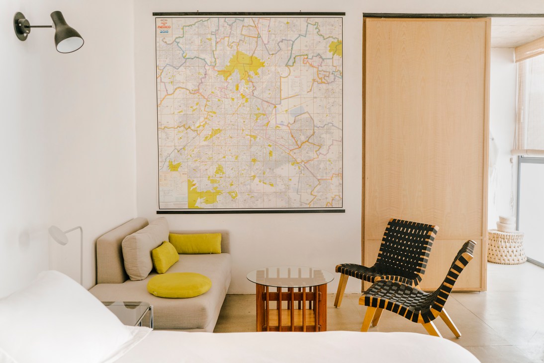 Modern living room with beige sofa, yellow cushions, woven chair, wall map, and wooden room divider