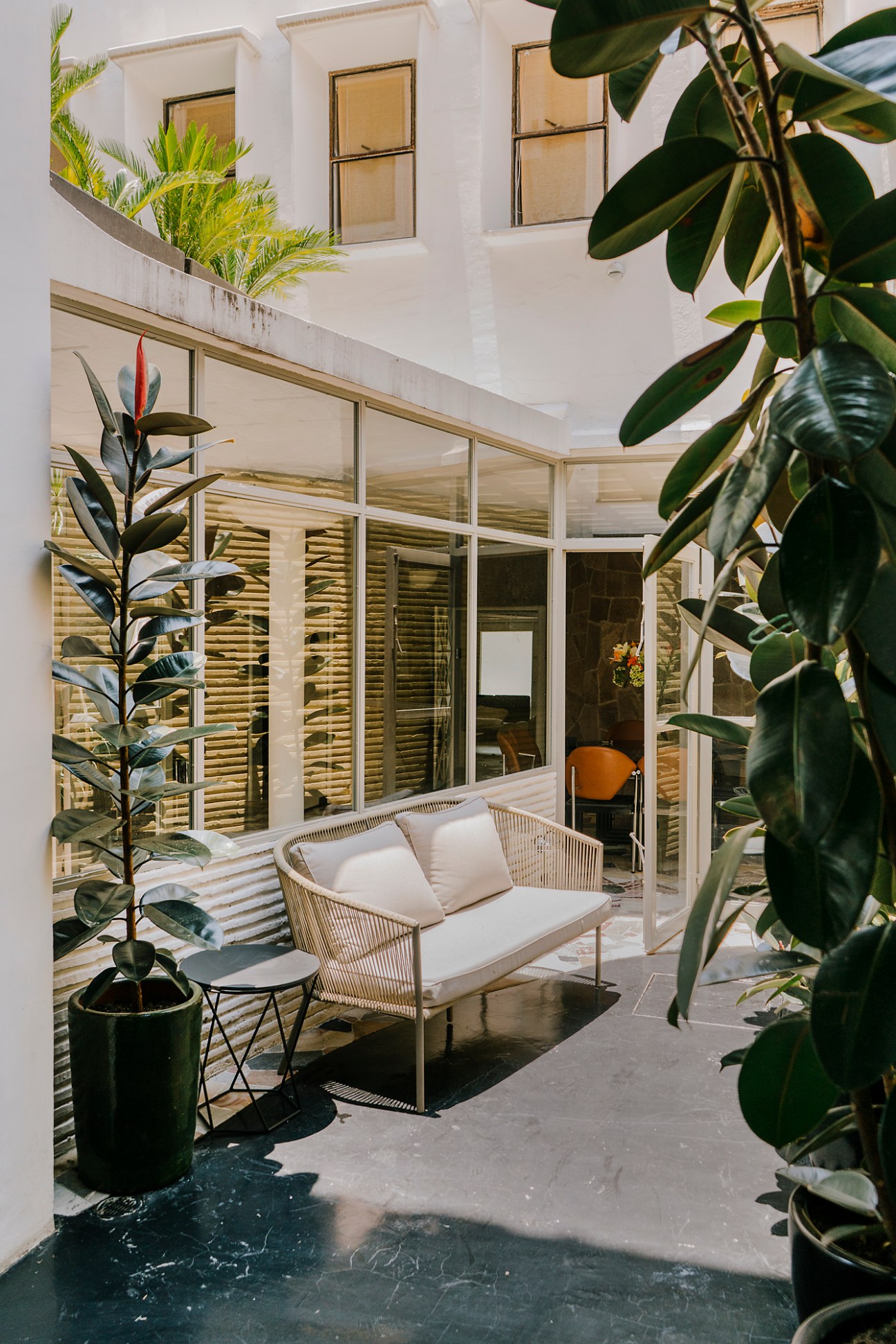 Modern courtyard seating area with wicker furniture, tropical plants, and glass-walled interior spaces