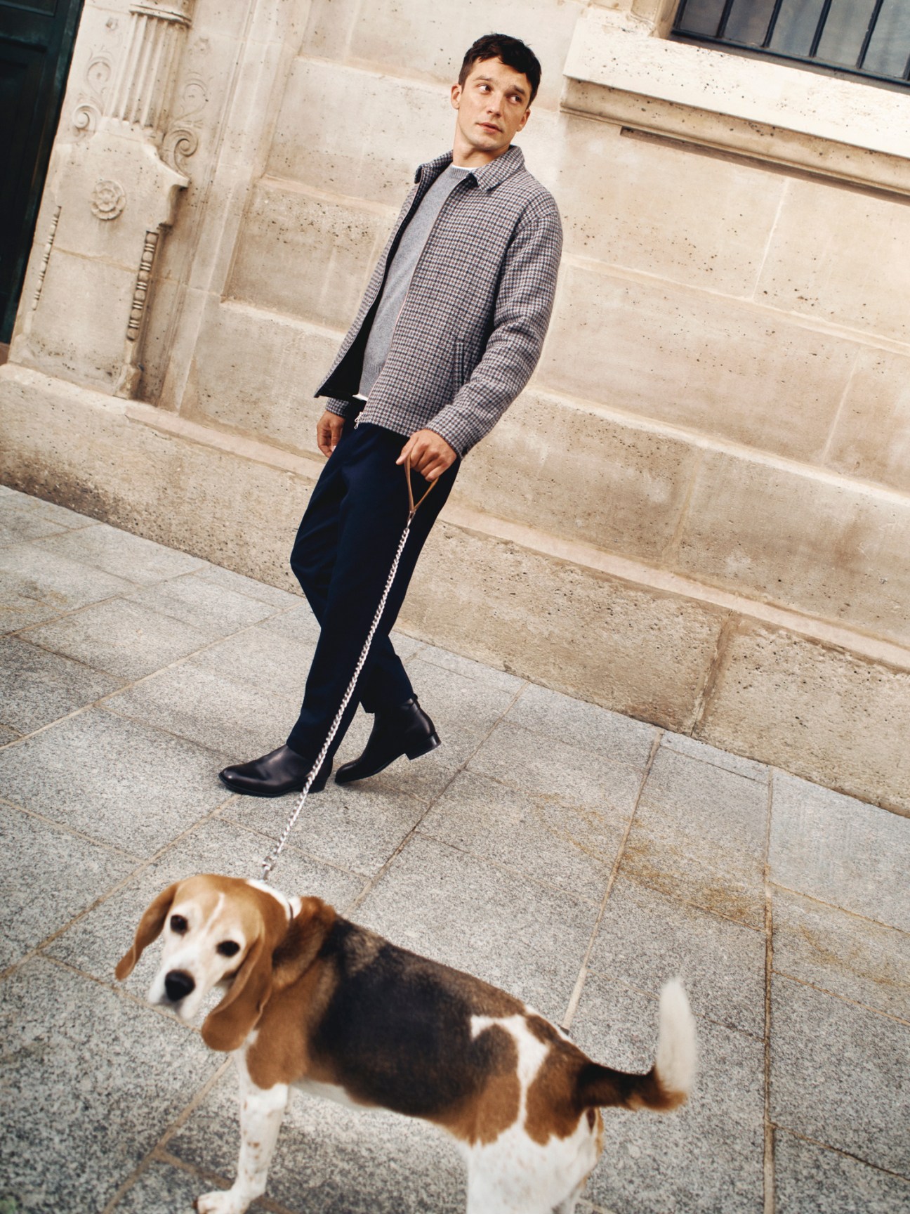 Model in checkered jacket over grey jumper walking beagle dog on leash outdoors