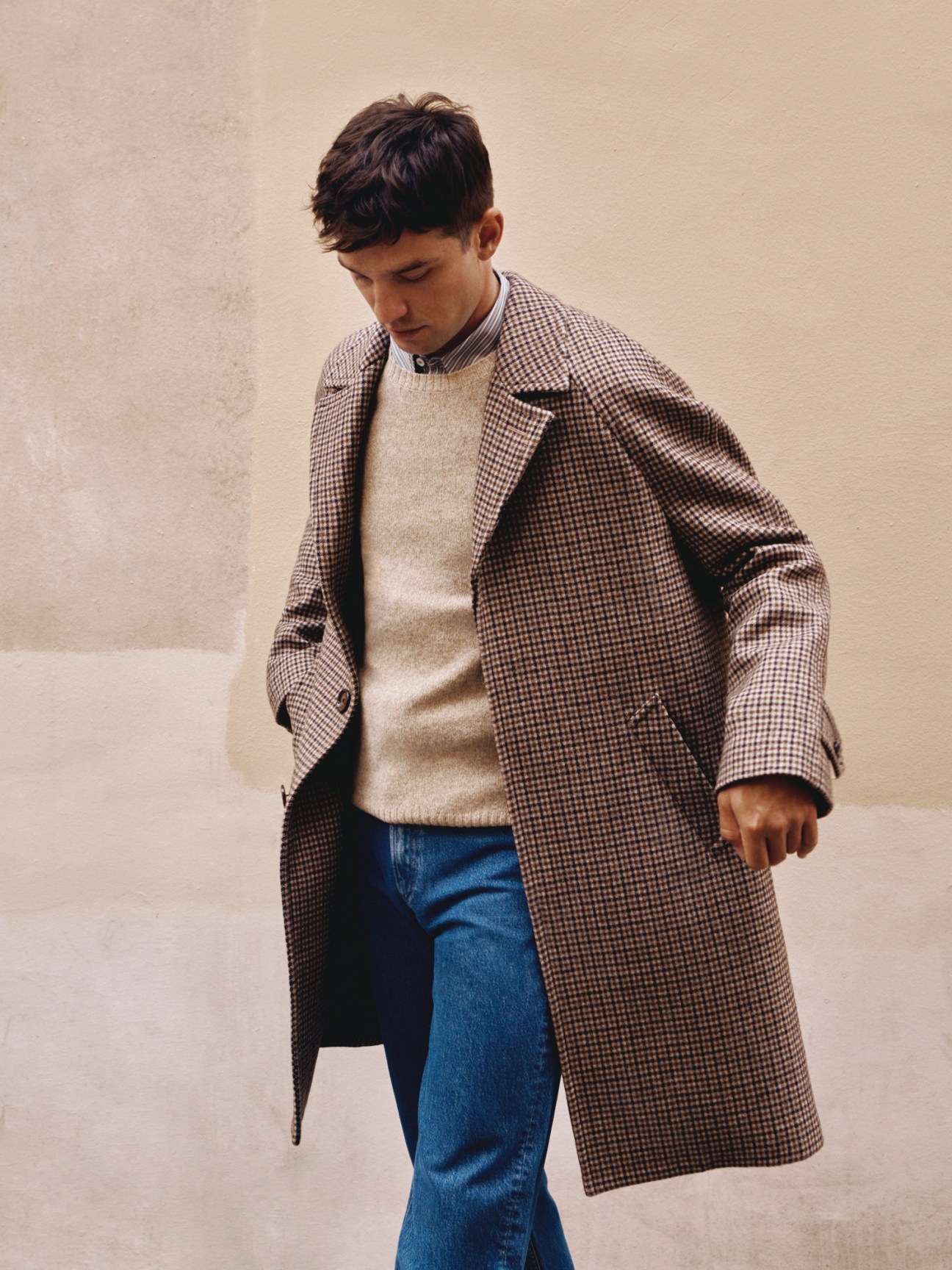 Model in long checkered coat over cream jumper with striped shirt and blue jeans