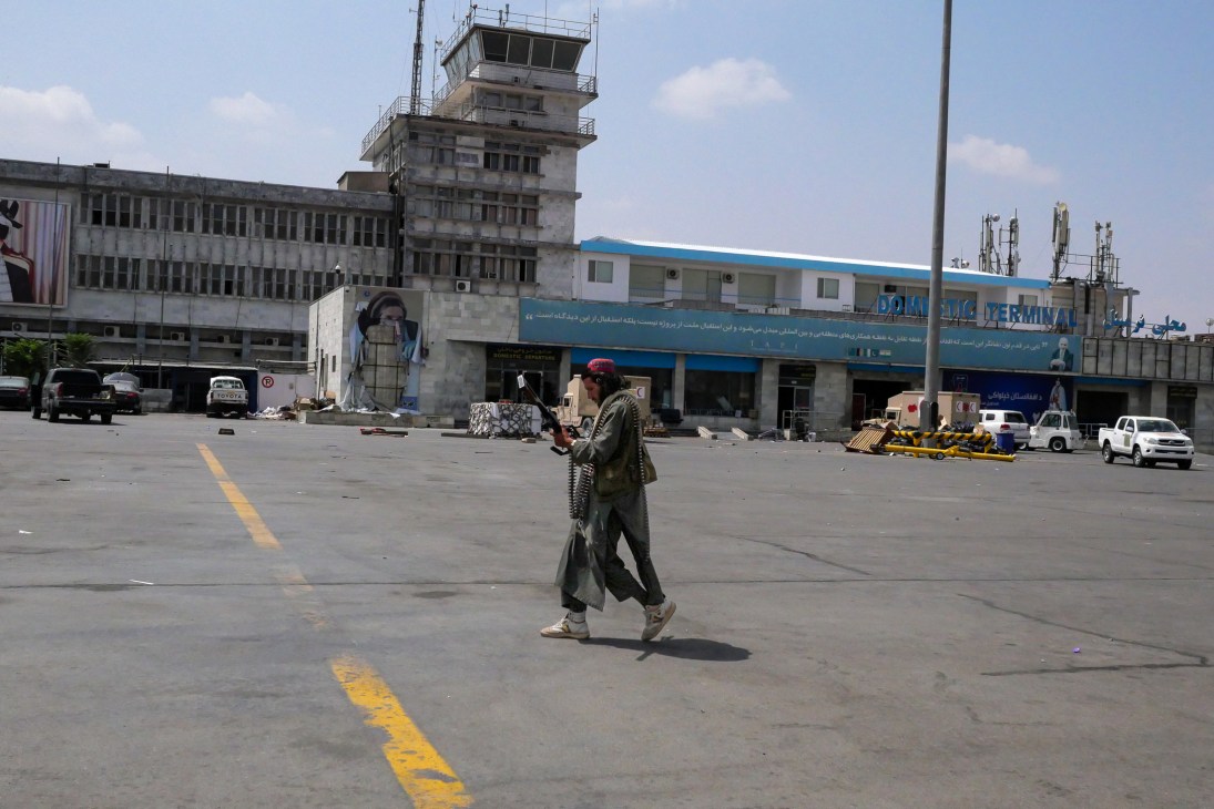Taliban fighter walking across airport tarmac carrying weapon with terminal building in background