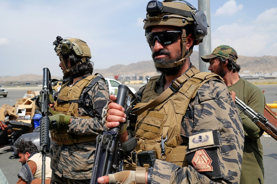 Taliban forces in military fatigues and tactical gear standing with weapons at what appears to be an airport