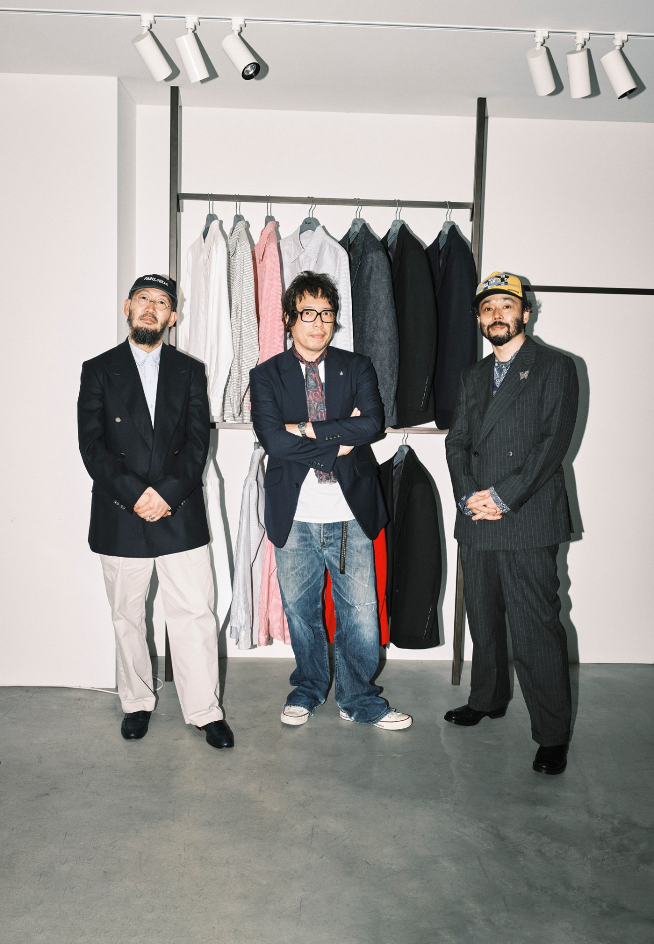 Three men in suits standing in front of clothing rack in minimalist white showroom