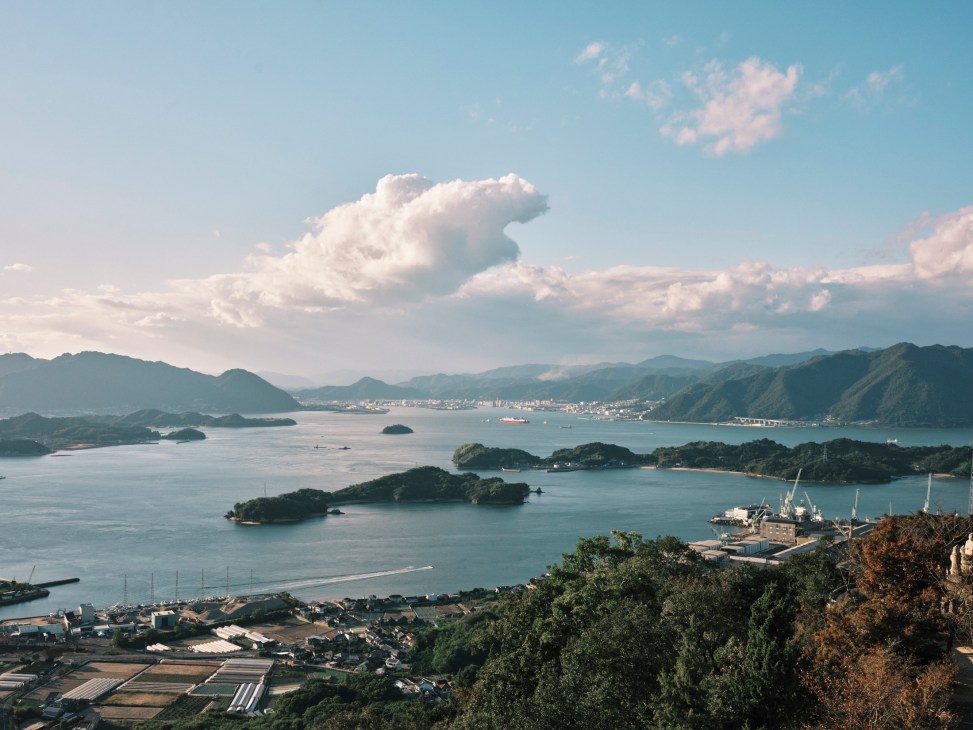 Aerial view of Onomichi, Japan showing Seto Inland Sea with islands, boats, and shipyards surrounded by mountains.