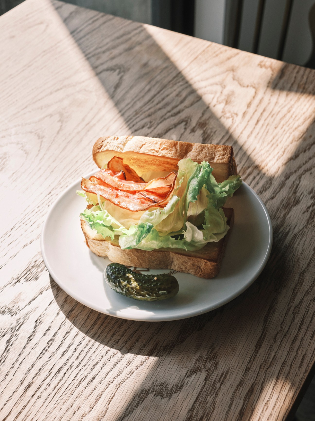 Sandwich with bacon, lettuce and pickles on a white plate on wooden table