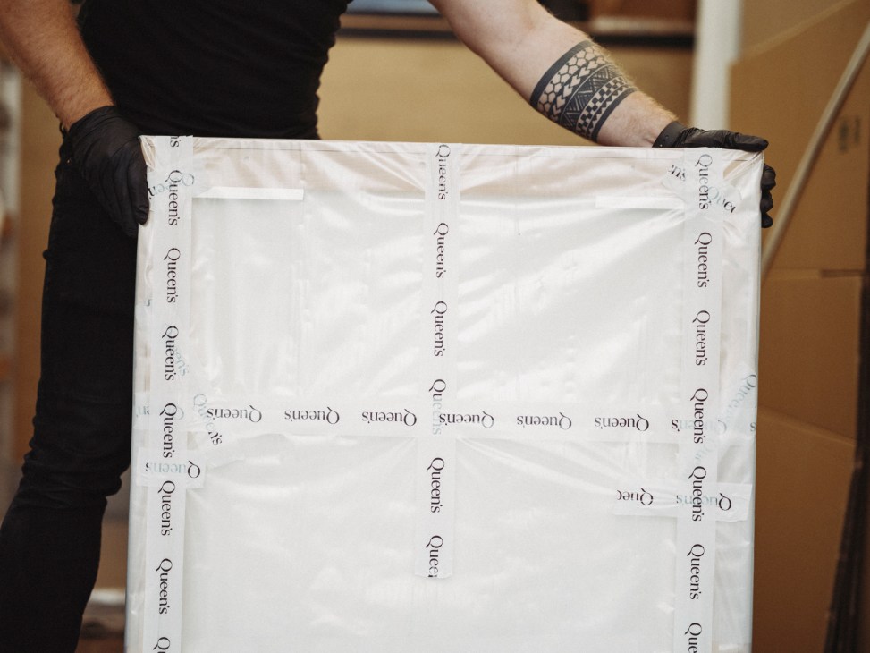 Worker in black gloves handling Queen's branded protective packaging material in art logistics facility