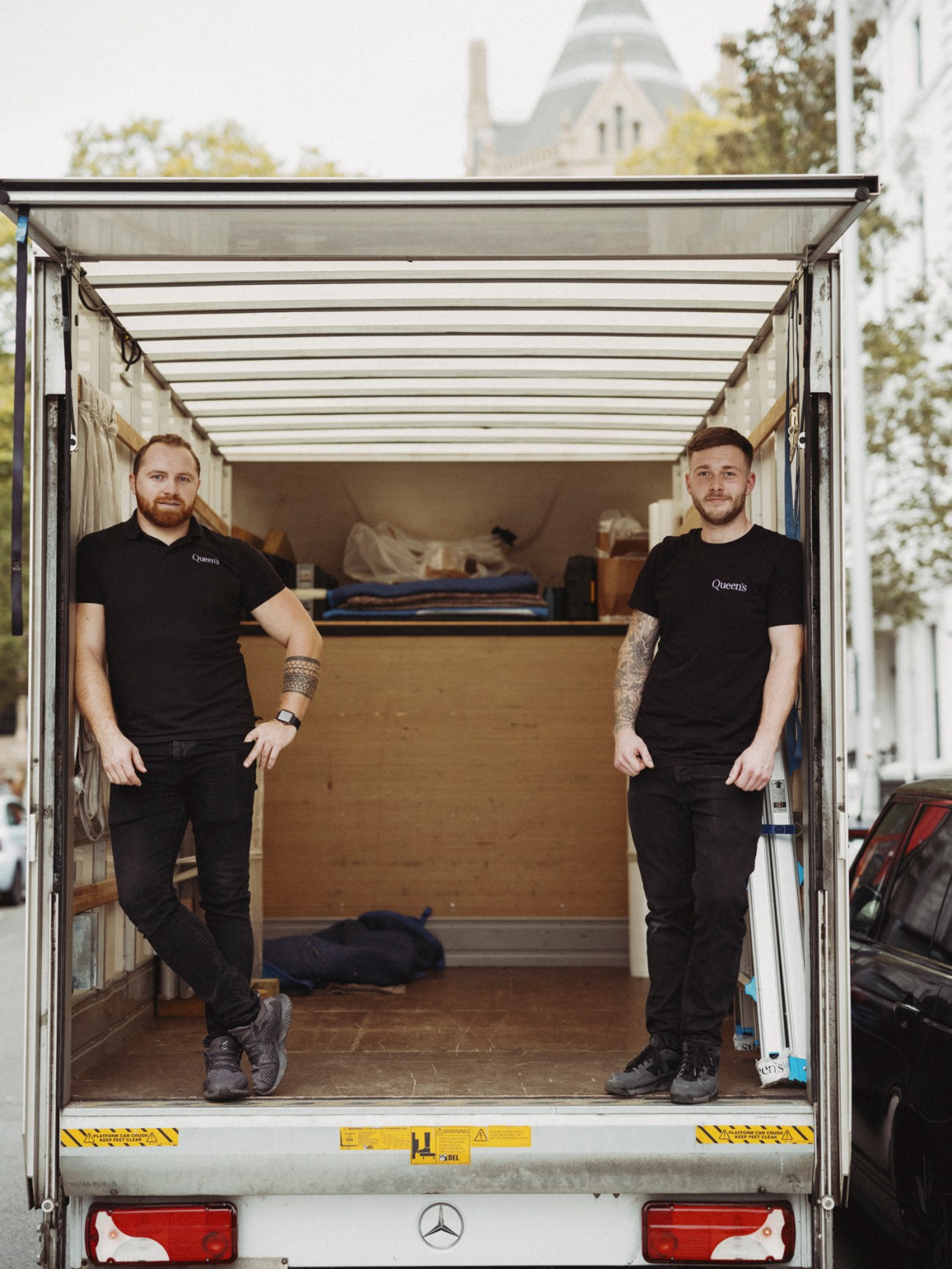 Two Queen's art logistics workers standing in the back of their delivery truck with art handling equipment