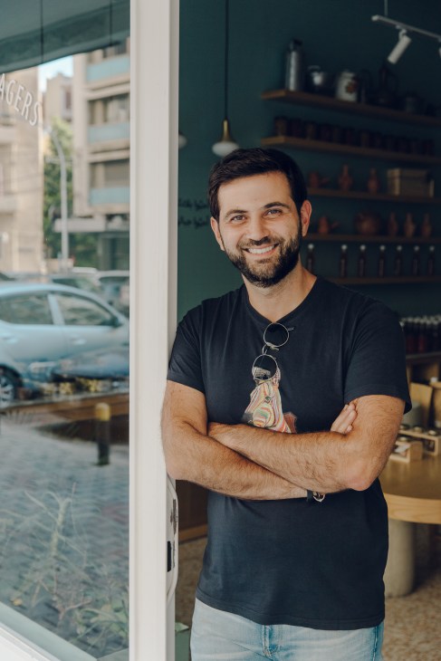 Kamel Taha, founder of Beirut food shop Feryal, smiling at the entrance of his store with shelves visible behind him.