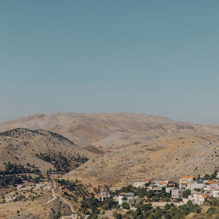 Mountainous Bekaa valley landscape with white buildings scattered among green vegetation and rolling hills under clear sky.
