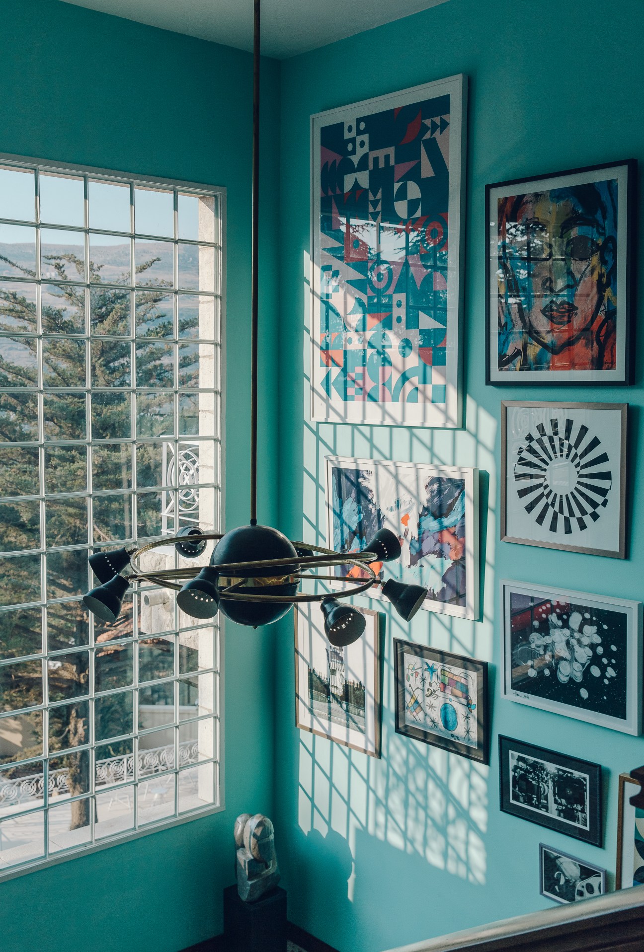 Turquoise salon with framed abstract and pop art on walls, vintage chandelier, large window overlooking Lebanese mountains.