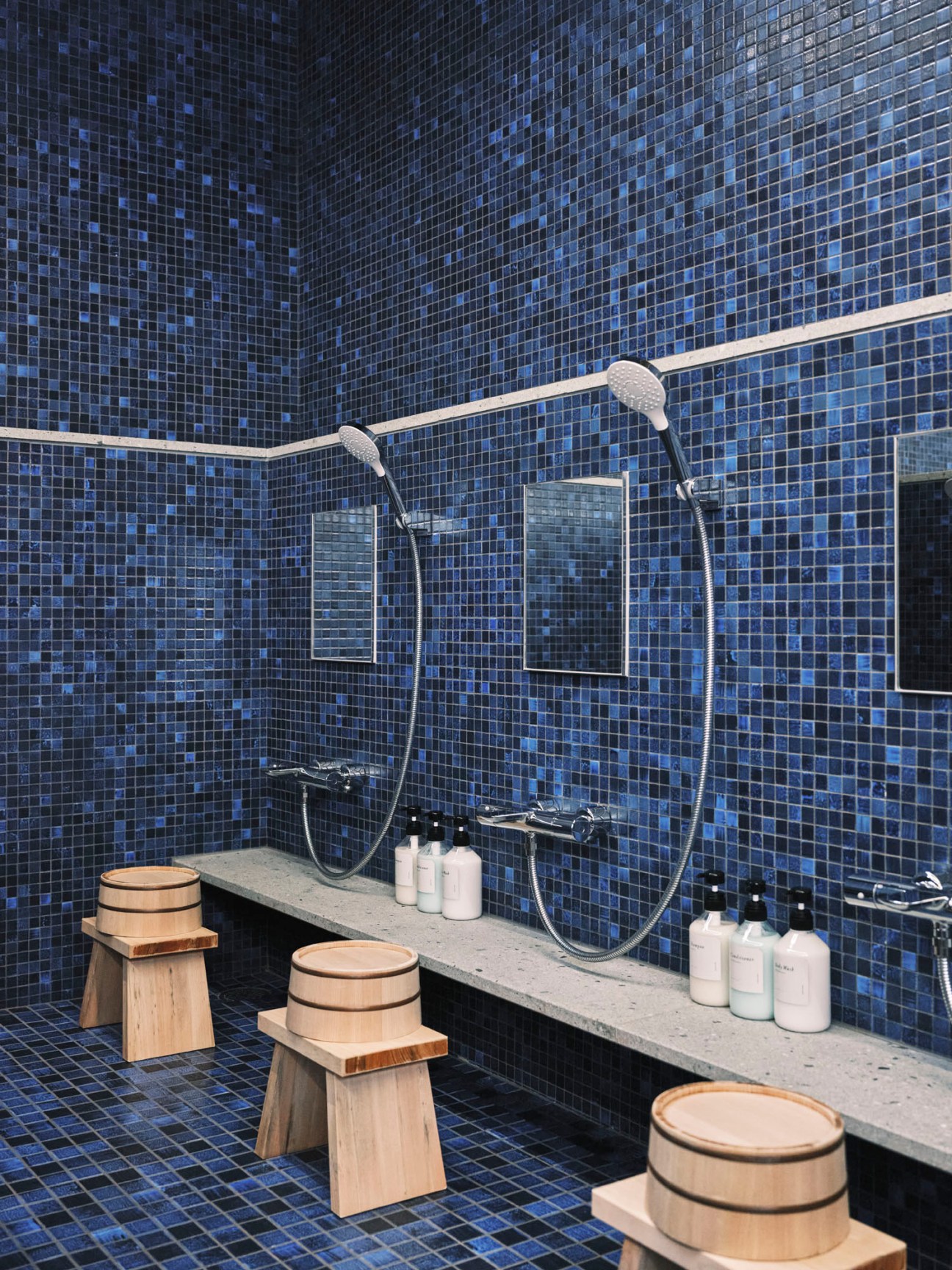 Blue mosaic tiled shower area with wooden stools and bath buckets at Yubune bathhouse