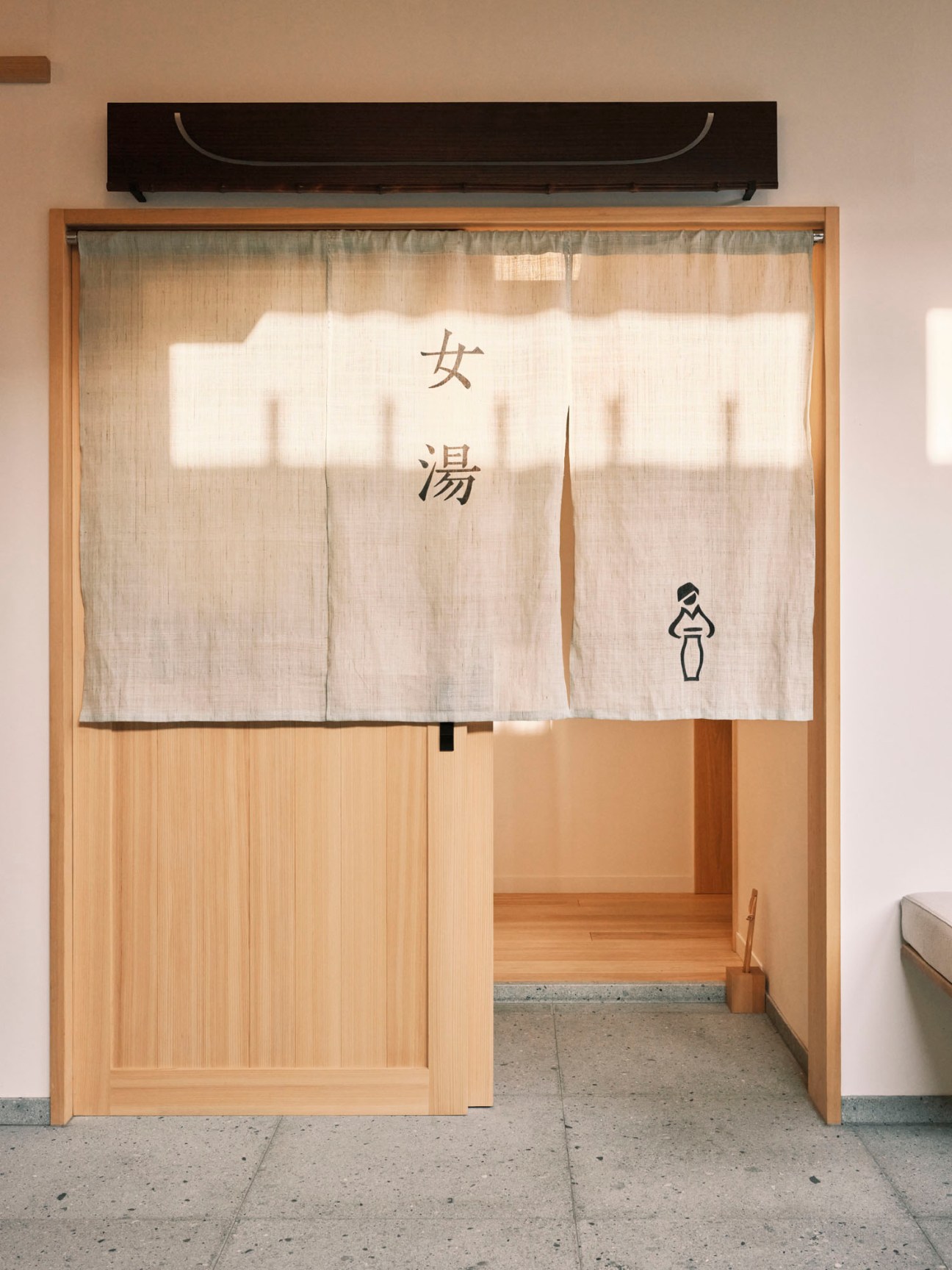 Traditional Japanese bathhouse entrance with white noren curtain displaying kanji characters and wooden doorway