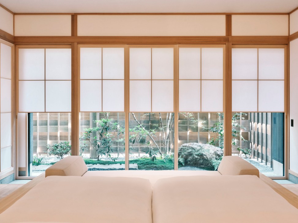 Minimalist Japanese hotel bedroom with wooden bed frame, neutral tones, and garden view through large windows