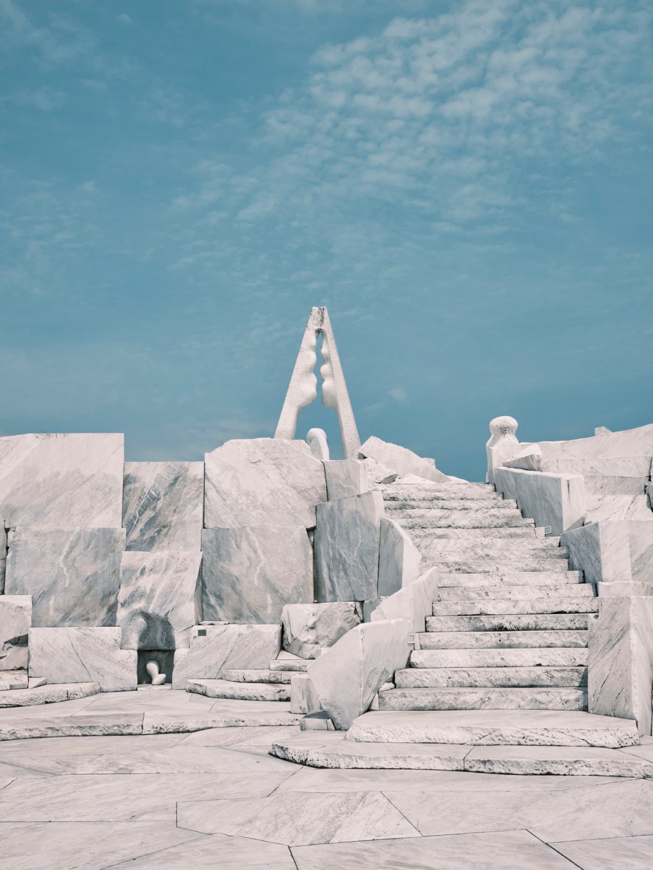 White marble sculptural installation with stepped geometric forms and tall triangular elements against blue sky