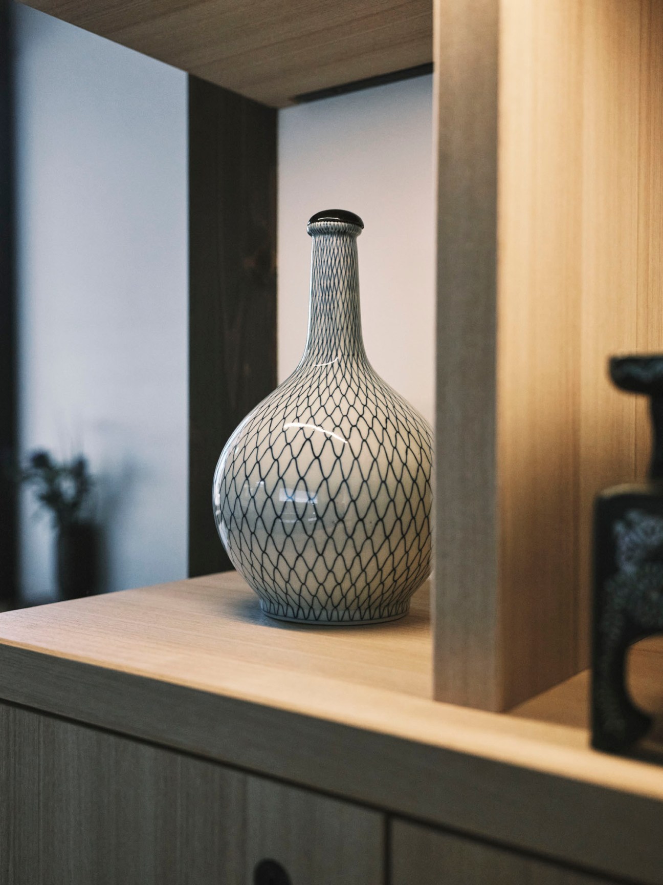 White ceramic vase with black diamond lattice pattern displayed on wooden shelf