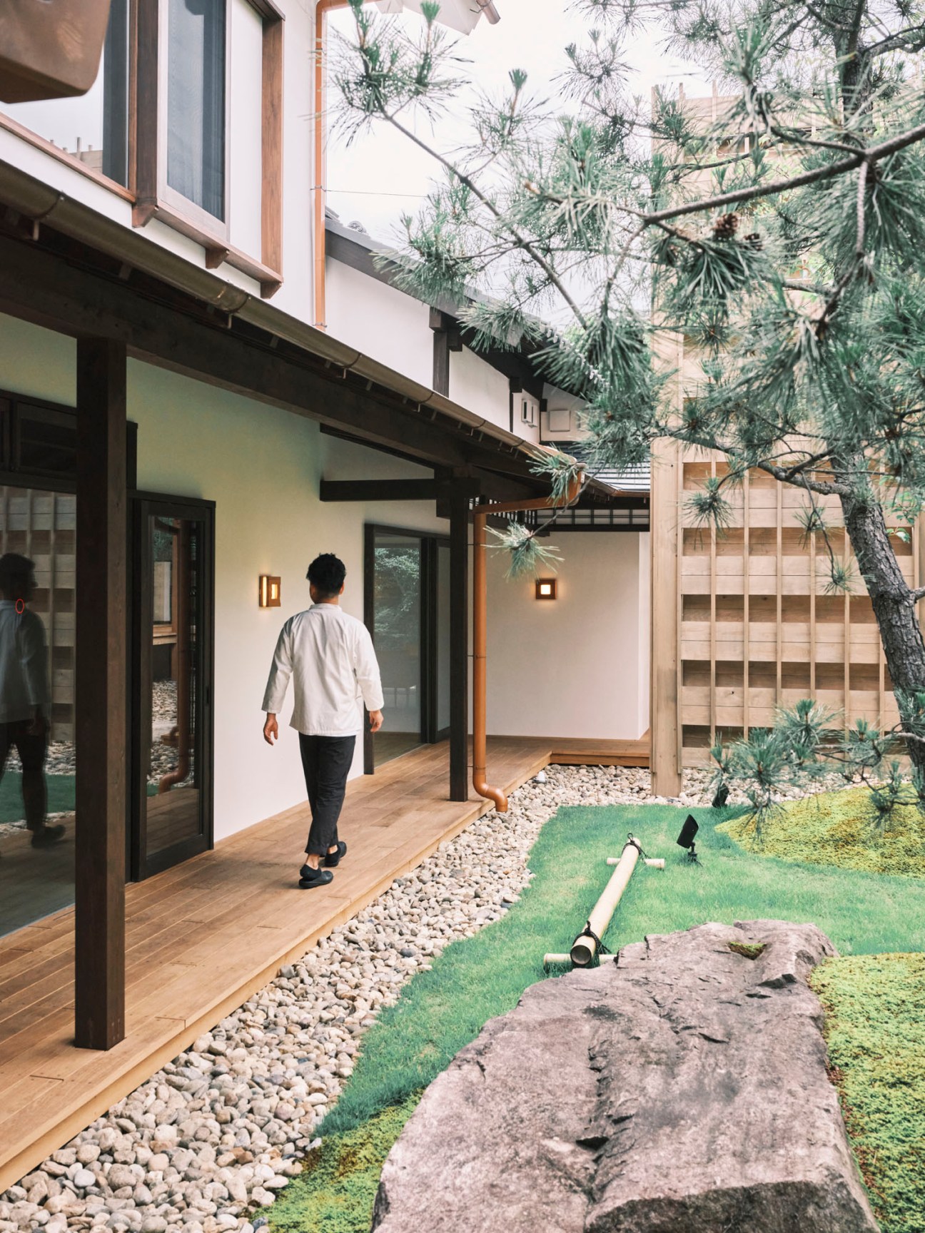 Person in white shirt walking on wooden deck of Japanese hotel with courtyard garden featuring rocks and traditional fence
