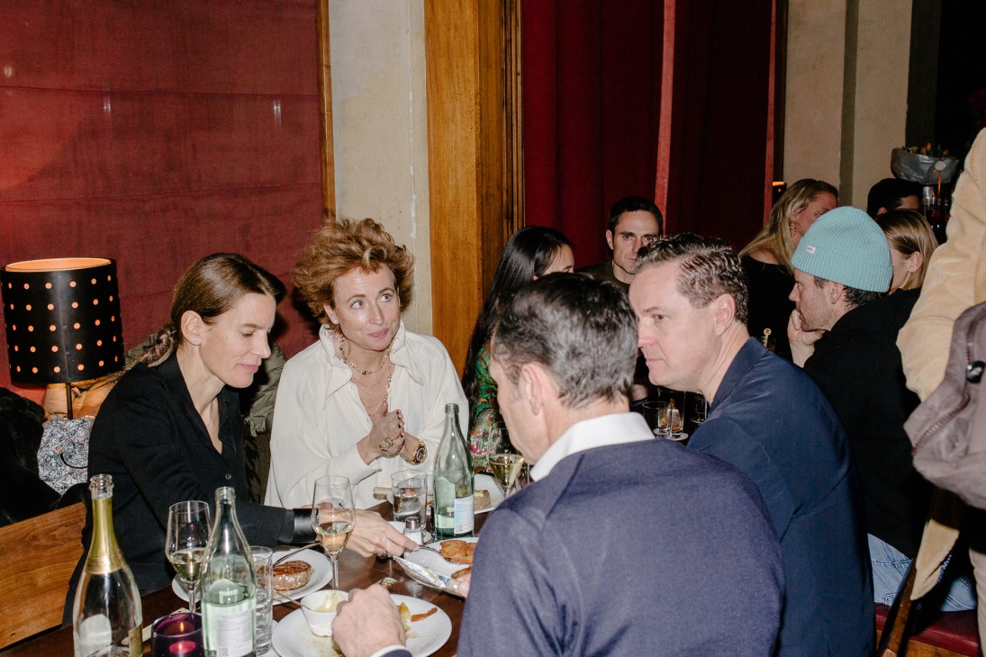 Diners gathered around a table in conversation at Schumann's bar in Munich, with wine bottles and glasses visible