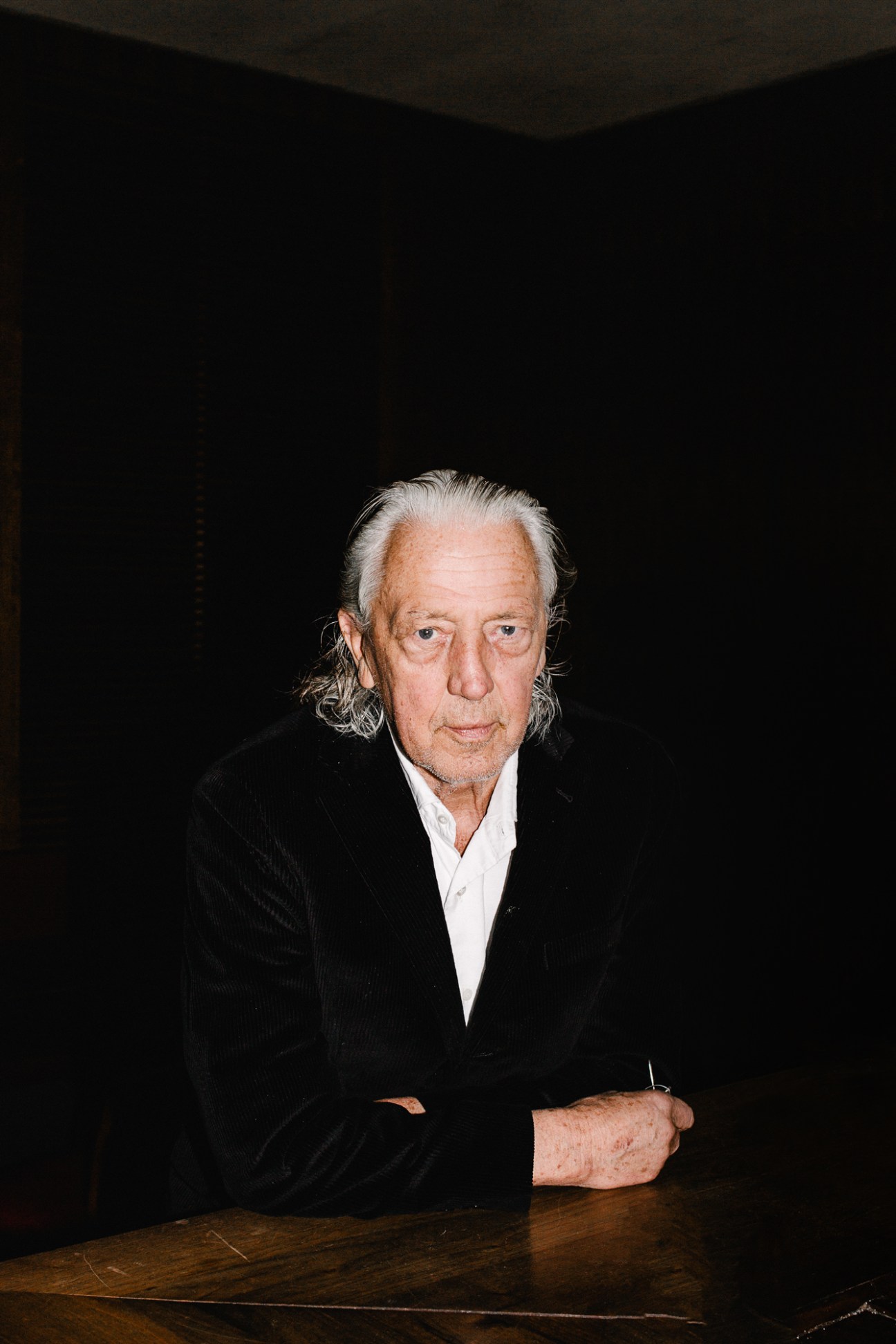 Charles Schumann in black velvet suit and white shirt sitting at a wooden table in dimly lit restaurant
