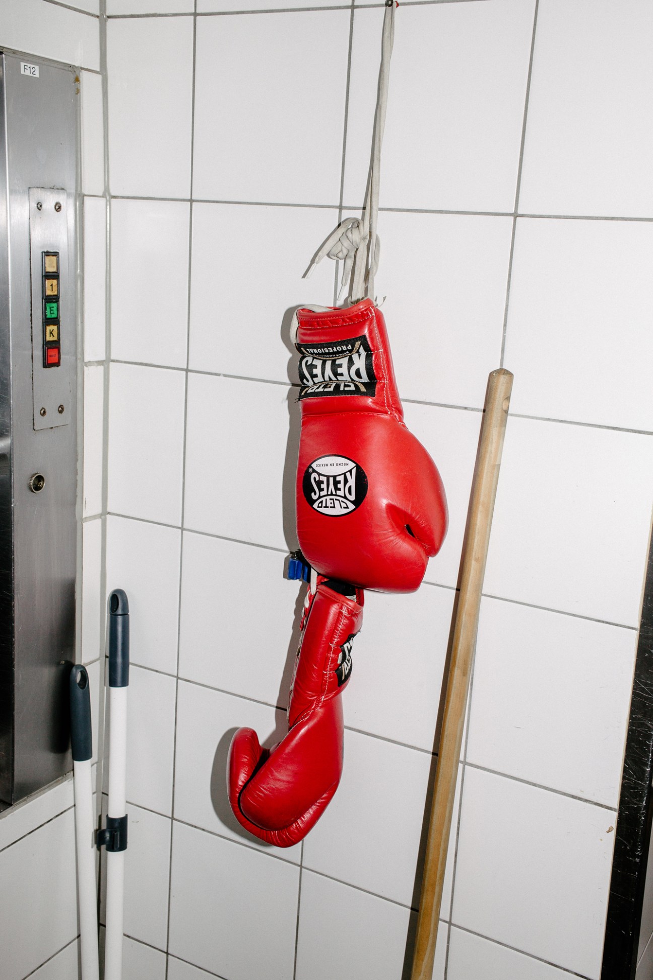 Red boxing gloves hanging on a hook against white tiled wall
