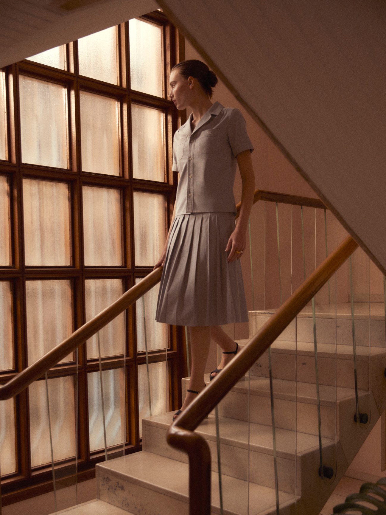 Woman in grey outfit walking down stairs by large window with natural lighting