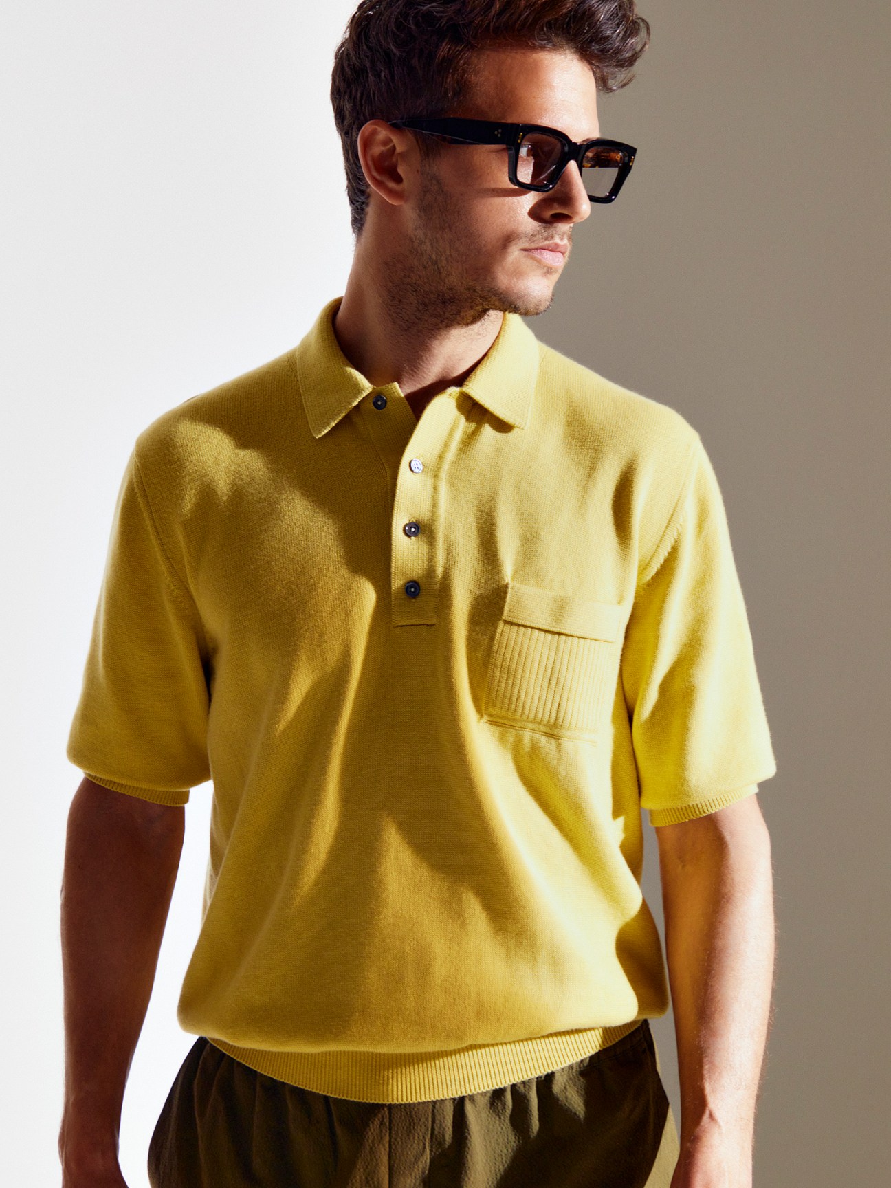 Man wearing yellow knitted polo shirt with collar and pocket, paired with trousers and sunglasses