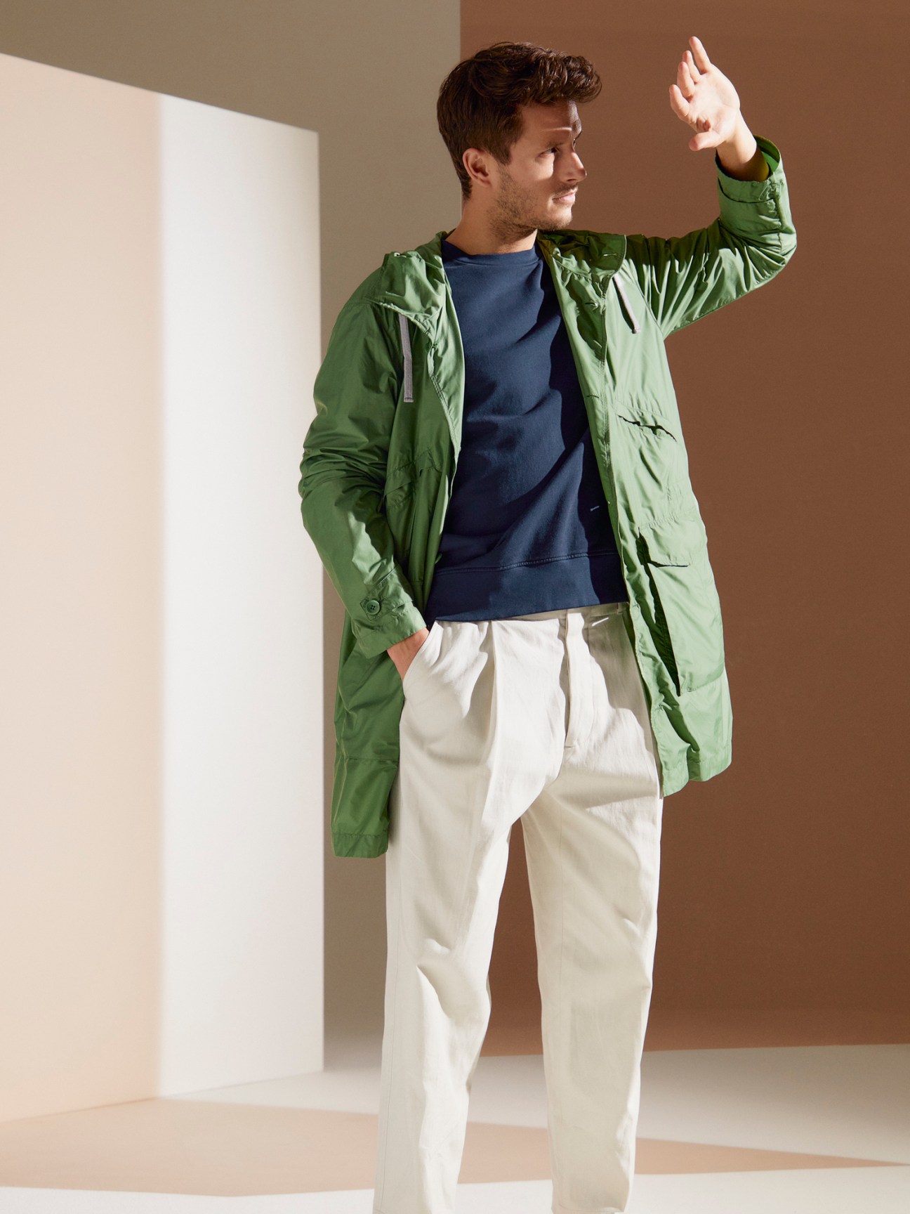 Man wearing green Herno Globe raincoat with navy sweatshirt and light trousers