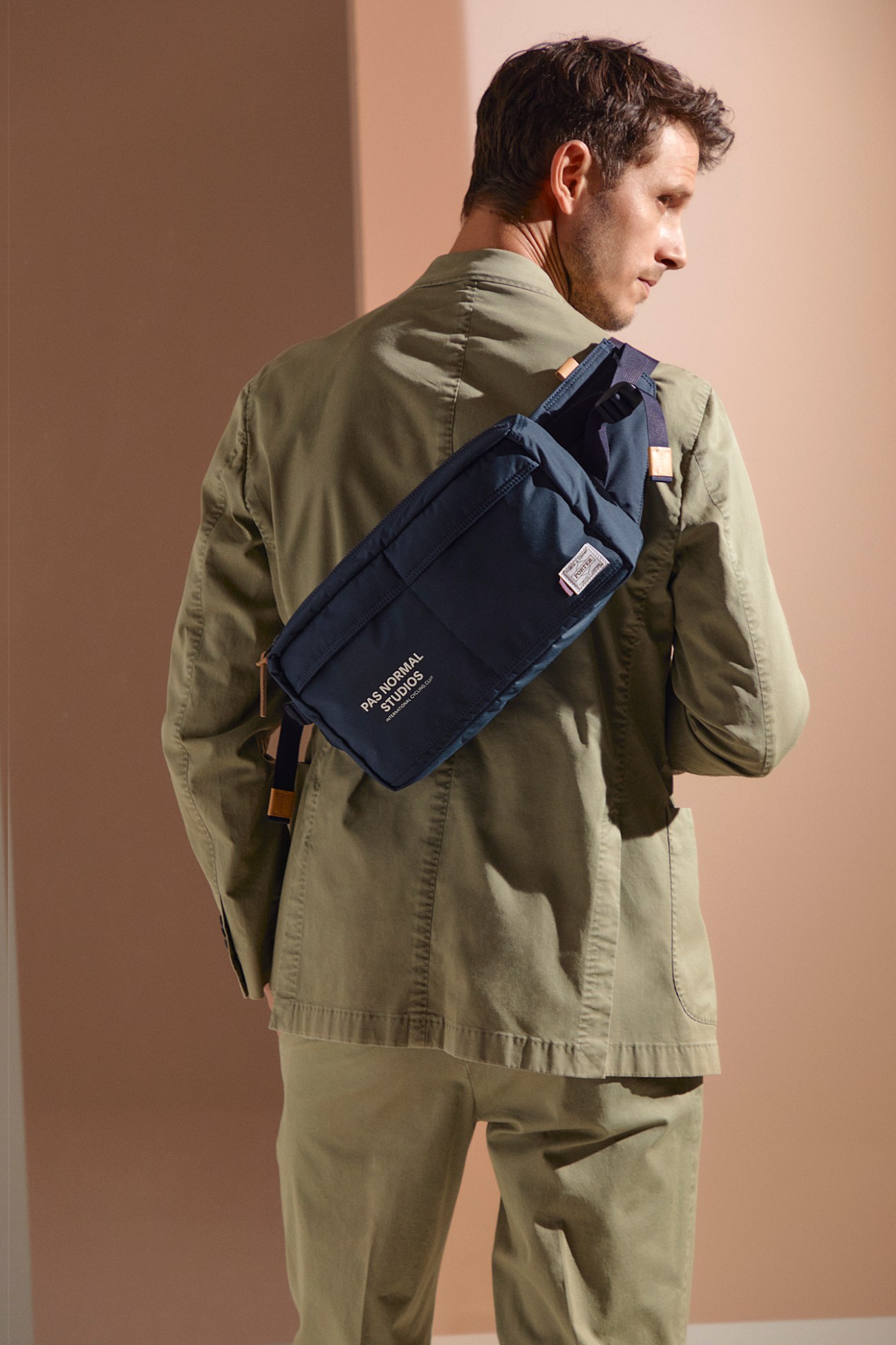 Man wearing navy jacket and trousers with Pas Normal Studios waist bag