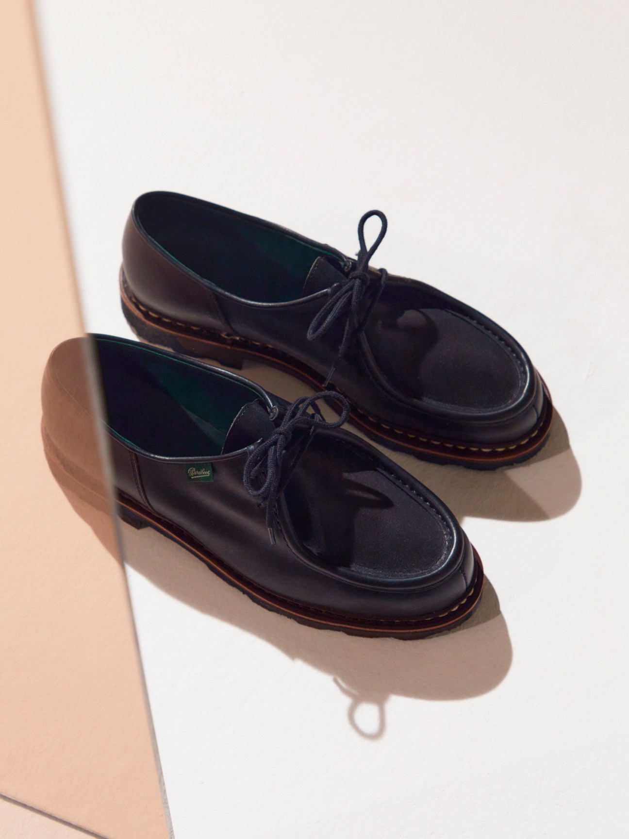 Black leather Paraboot derby shoes with contrasting brown sole stitching on beige surface