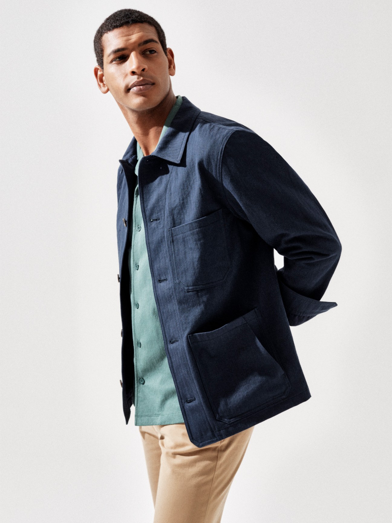 Model wearing navy work jacket over mint green shirt with beige trousers