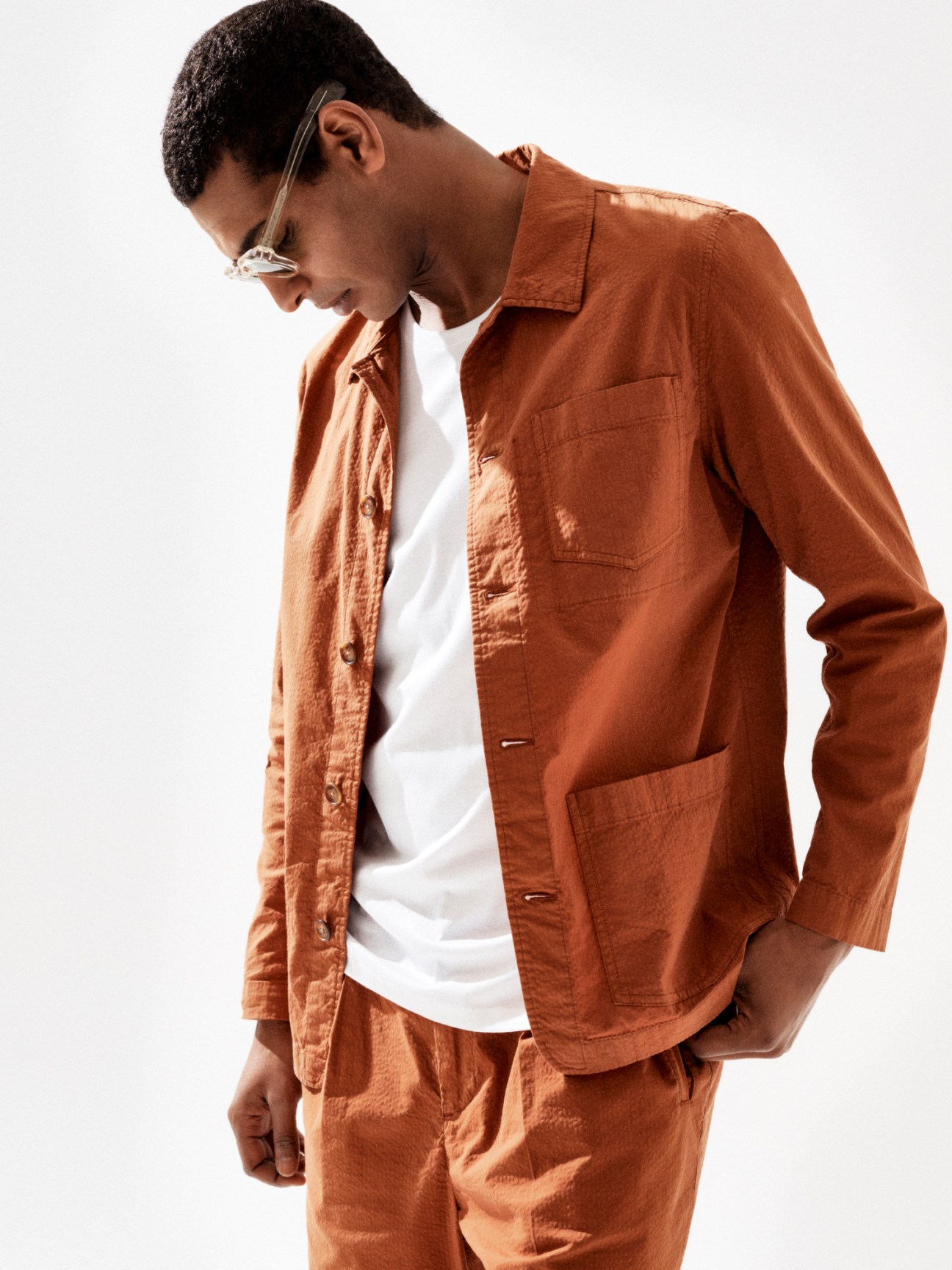 Model wearing beige jacket and trousers with white t-shirt and sunglasses