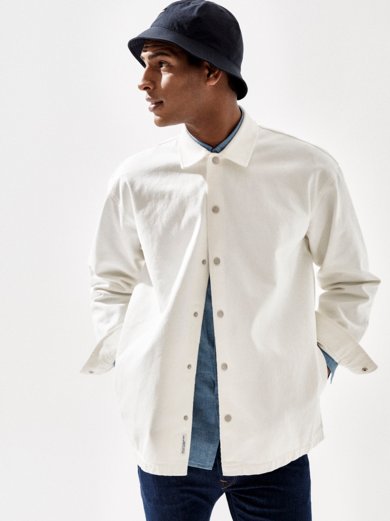 Model wearing white button-up shirt with dark bucket hat and jeans in casual spring styling