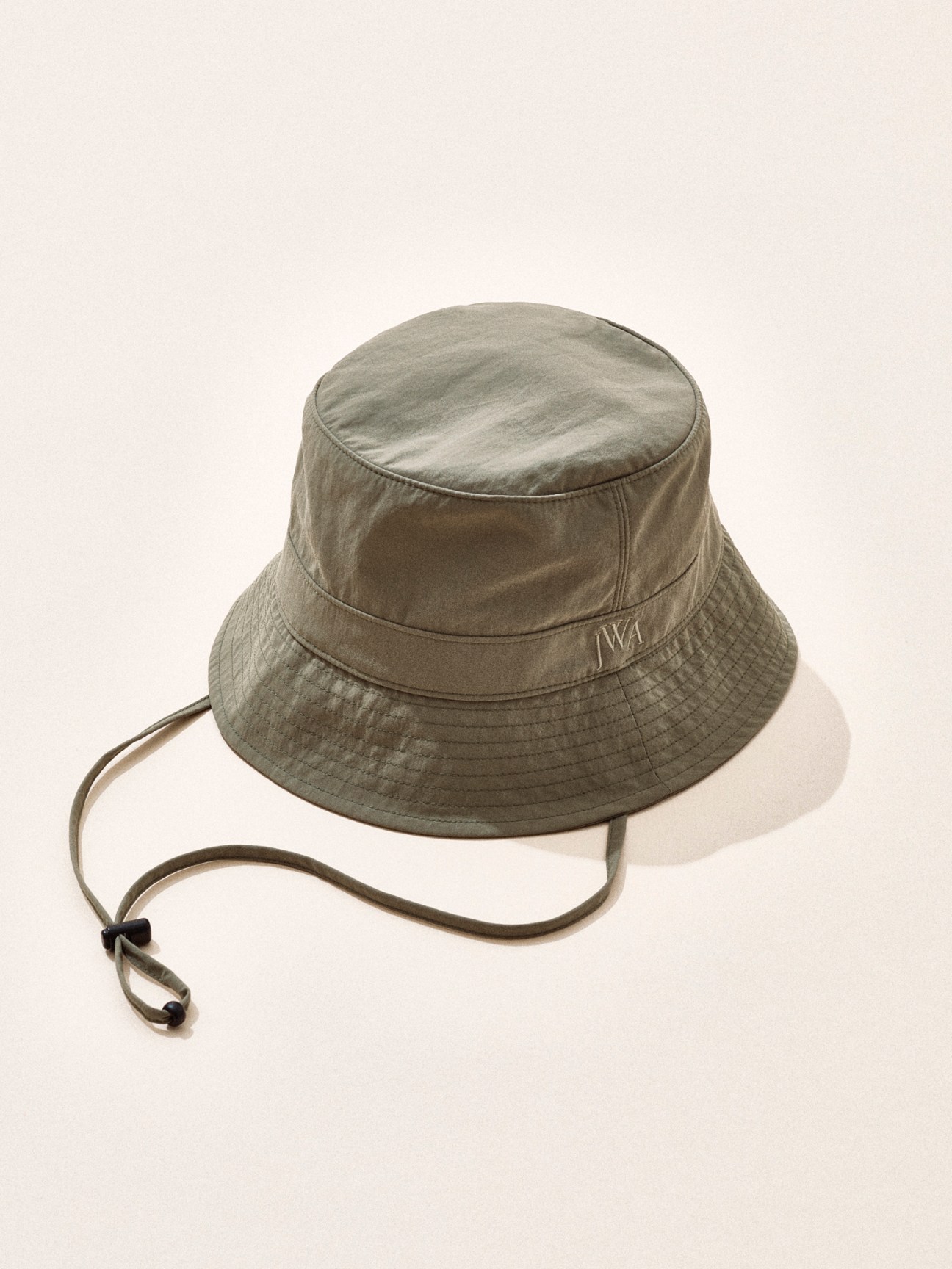 Olive green bucket hat with chin strap and JW Anderson branding on neutral background